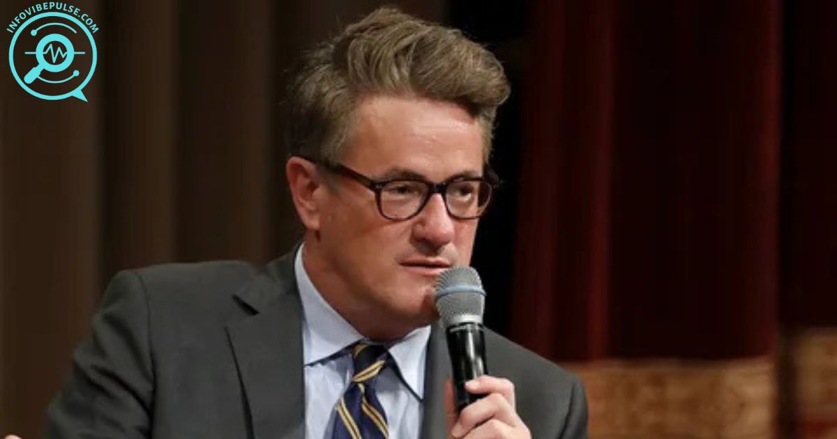 Joe Scarborough speaking at an event, holding a microphone, wearing glasses and a suit
