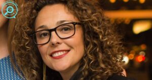 Rishia Haas smiling in a leather jacket and glasses at an evening event, 2025.